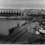 Photograph shows passengers and cargo on the wharf at Arica, Chile (formerly Peru), with mountains in the background.